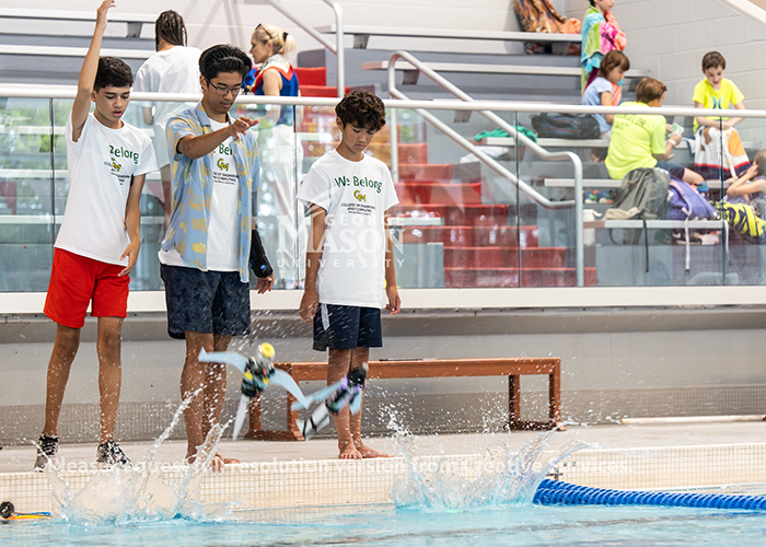 Students by the pool drop their robots into the water