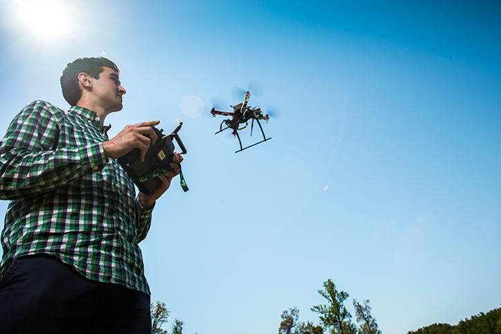 A student outside under a clear blue sky flying a medium sized drone.