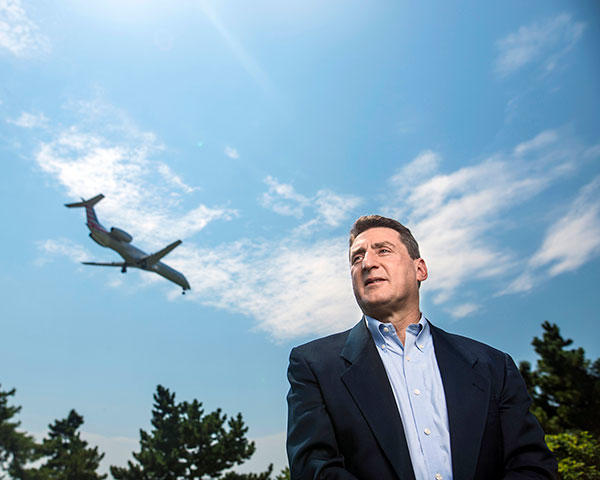 Lance Sherry standing outside with a bright blue sky and a plane flying through the air.
