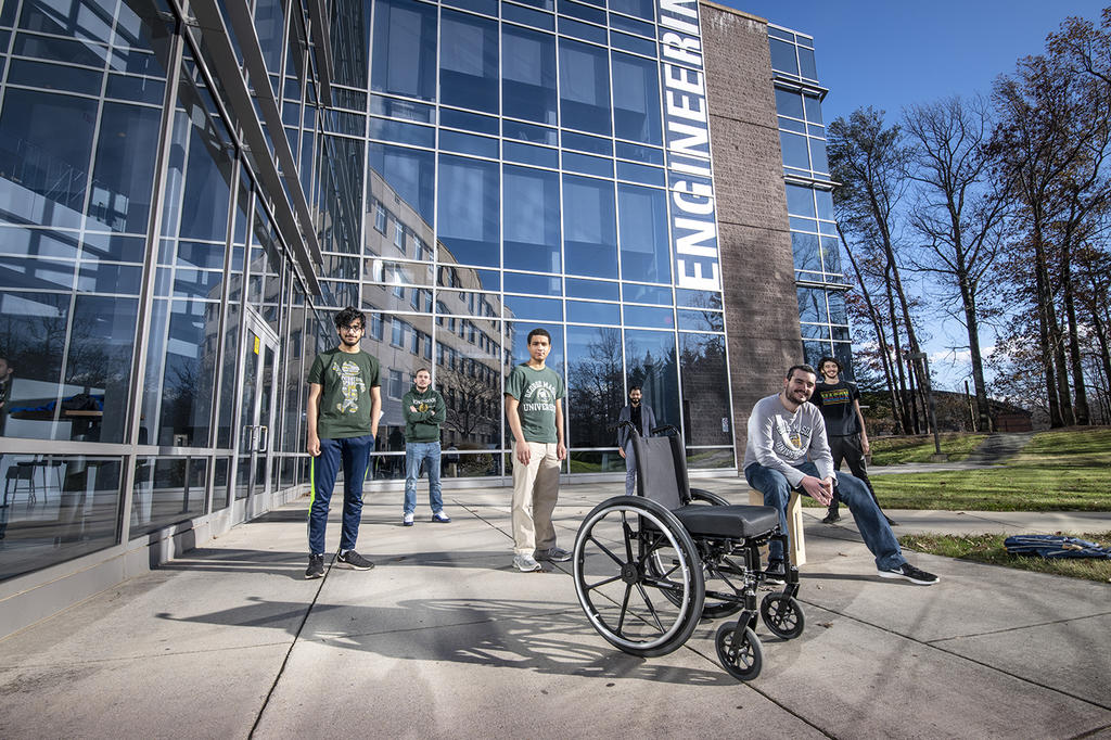 Students standing around outside looking at the camera, the wheelchair they designed in the middle of the frame.