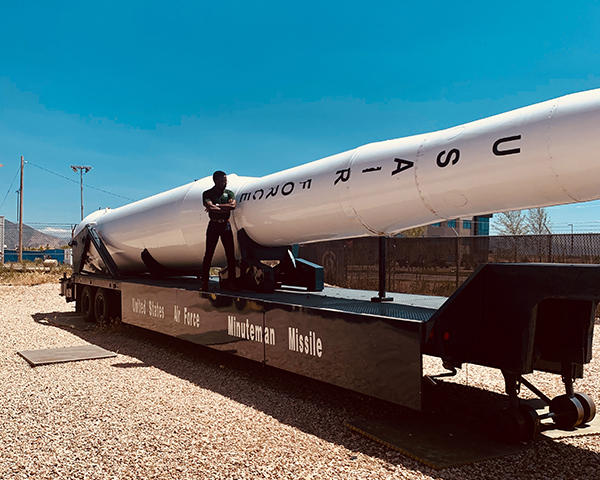 Chigozie Erondu standing in front of a missile that is propped up long-ways on a big metal stand that reads "Minuteman Missile."