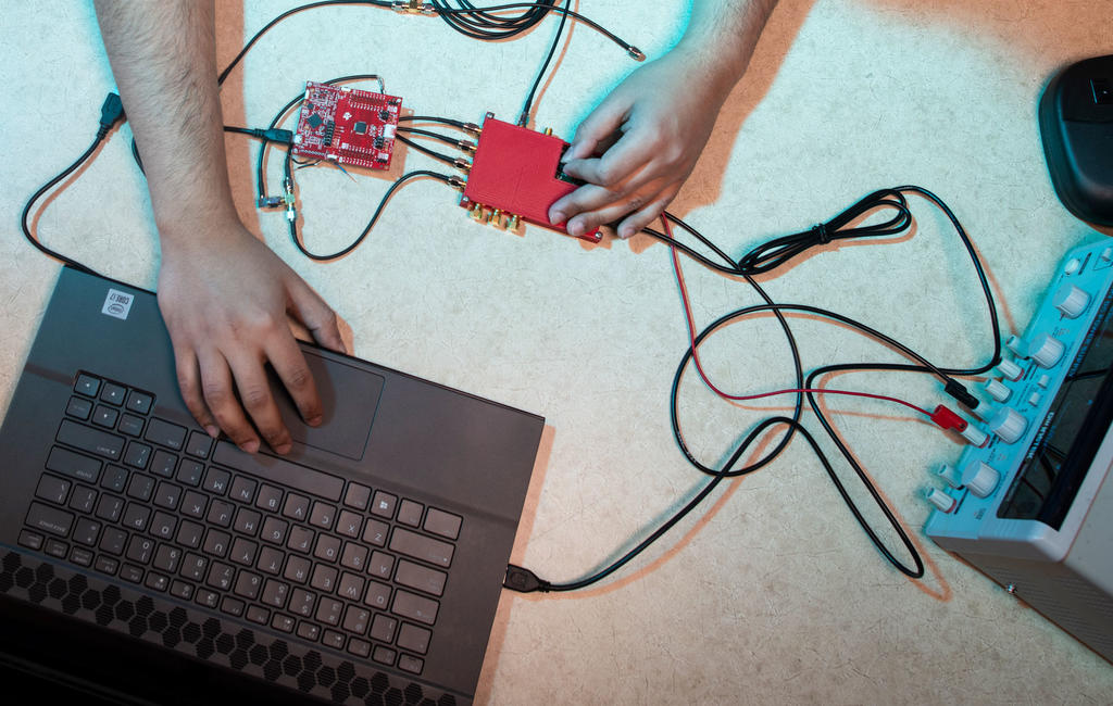 Hands of a male student operating an electric circuit which is connected to a computer.