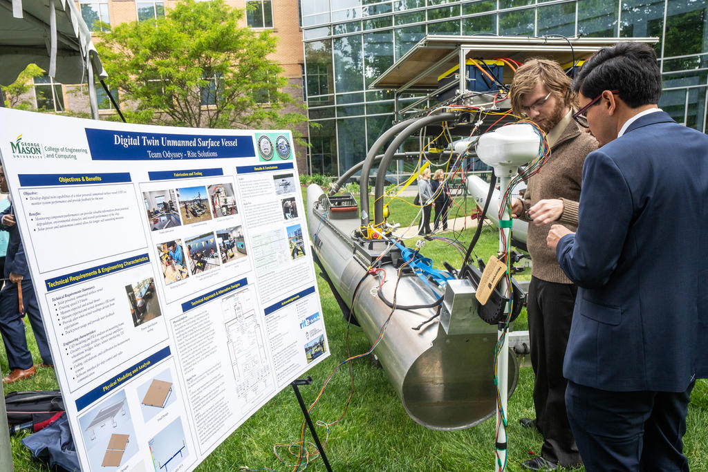 Two male students demonstrate their autonomous surface vessel on the lawn of the Nguyen Engineering Building