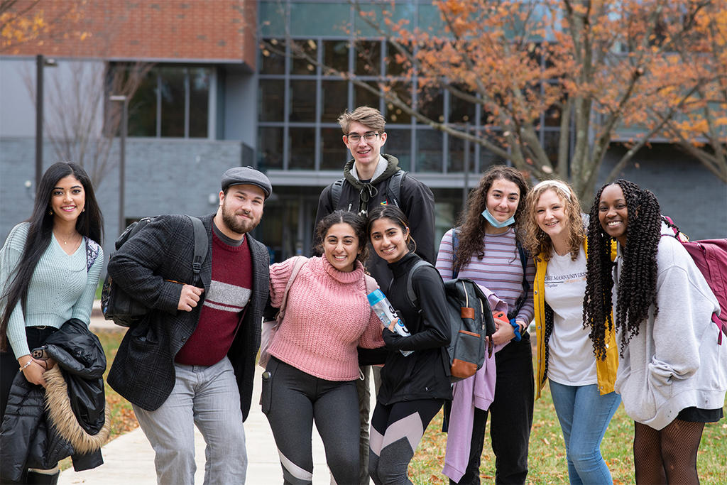 A diverse group of students smile in front of a building on George Mason's Fairfax Campus