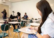 Students in classroom take notes by hand in notebooks. 