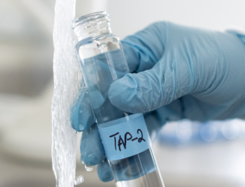 A gloved hand is holding a test tube under a flowing tap