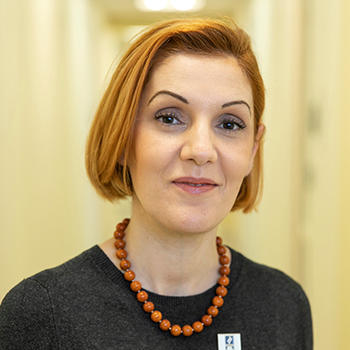 A woman in a gray top stands in front of a yellow background.