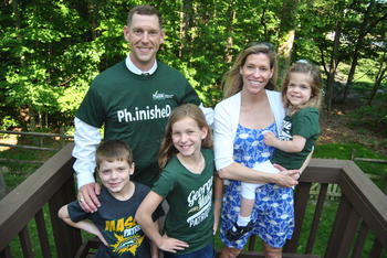 A man and wife pose in front of a forest backdrop with three young children