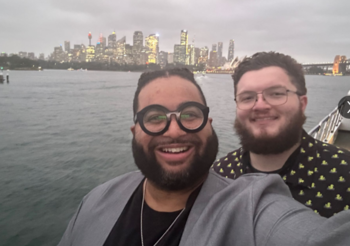 Two men take a selfie in front of the Sydney skyline
